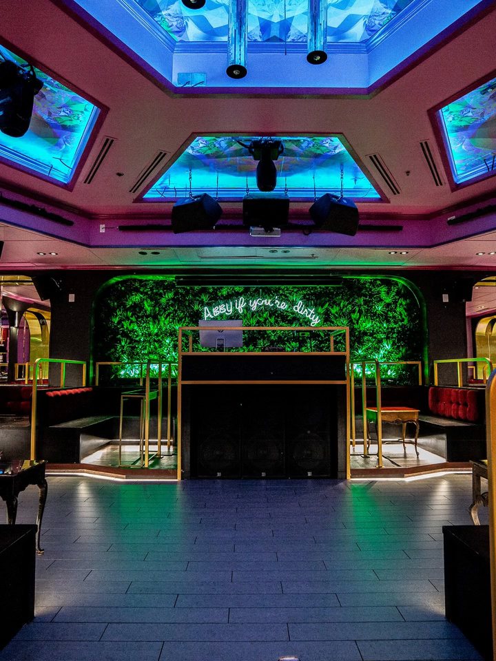 Abigail's main room, with the DJ booth against a green living wall, gold-arched booths on each side and lit ceiling panels